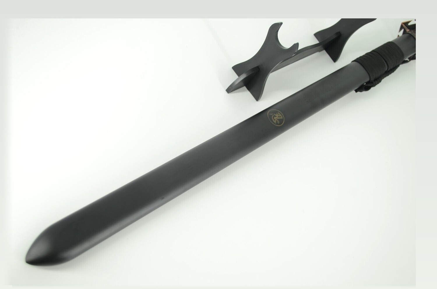 A traditional straight katana sword displayed on a wooden stand, shown in a dark studio with soft directional light emphasising the polished blade, wrapped handle and decorative scabbard.